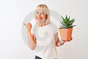 Middle age woman holding cactus pot standing over isolated white background pointing and showing with thumb up to the side with