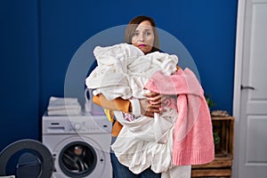 Middle age woman holding dirty laundry ready to put it in the washing machine relaxed with serious expression on face