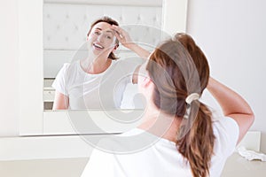 Middle age woman looking in mirror on face wrinkle forehead in bedroom. Wrinkles and anti aging skin care concept. Selective focus