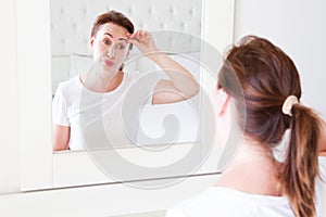 Middle age woman looking in mirror on face wrinkle forehead in bedroom. Wrinkles and anti aging skin care concept. Selective focus