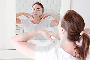 Middle age woman looking in mirror on face. Wrinkles and anti aging skin care concept. Selective focus