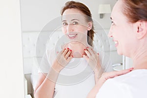 Middle age woman looking in mirror on face. Wrinkles and anti aging skin care concept. Selective focus