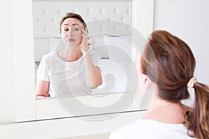 Middle age woman looking in mirror on face. Wrinkles and anti aging skin care concept. Selective focus