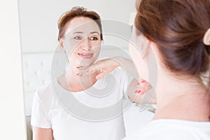 Middle age woman looking in mirror on face. Wrinkles and anti aging skin care concept. Selective focus