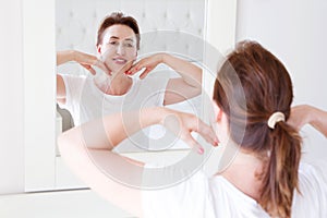 Middle age woman looking in mirror on face. Wrinkles and anti aging skin care concept. Selective focus