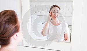 Middle age woman looking in mirror on face. Wrinkles and anti aging skin care concept. Selective focus