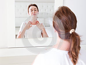 Middle age woman looking in mirror on face. Wrinkles and anti aging skin care concept. Selective focus