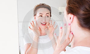 Middle age woman looking in mirror on face. Wrinkles and anti aging skin care concept. Selective focus. Banner