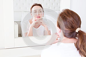 Middle age woman looking in mirror on face. Wrinkles and anti aging skin care concept. Selective focus