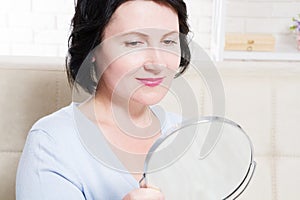 Middle age woman looking in mirror on face wrinkles at home background. Skin care and anti aging concept. Selective focus