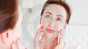 Middle age woman looking in mirror on wrinkle face on forehead. Menopause, Wrinkles and anti aging skin care concept. Selective