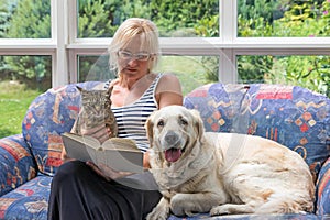 Middle age woman is reading a book with pets together