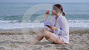 Middle age woman relaxing on beach in headphones with smartphone
