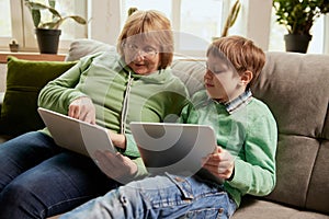 Middle age woman and school age boy, granny and grandson sitting at home and talking, having fun. Concept of emotions