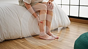 Middle age woman sitting on bed tired massaging legs at bedroom