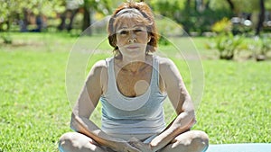 Middle age woman sitting on yoga mat with serious face at park