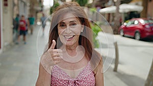 Middle age woman smiling confident doing ok sign with thumb up at street