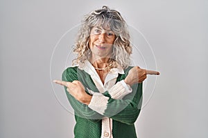 Middle age woman standing over white background pointing to both sides with fingers, different direction disagree