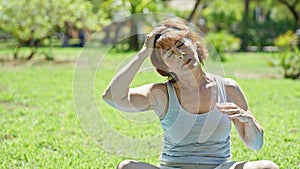 Middle age woman stretching head sitting on yoga mat at park