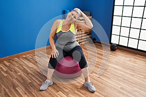 Middle age woman stretching neck sitting on fit ball at sport center