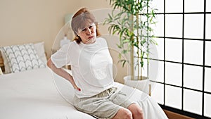 Middle age woman suffering for back injury sitting on bed at bedroom