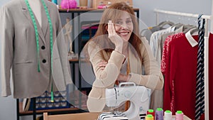 Middle age woman tailor smiling confident leaning on sewing machine at clothing factory