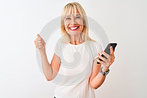 Middle age woman using smartphone standing over isolated white background happy with big smile doing ok sign, thumb up with