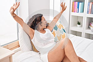Middle age woman waking up stretching arms at bedroom