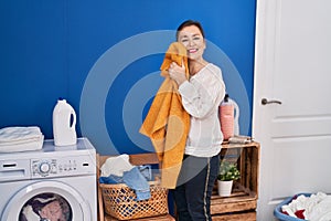 Middle age woman washing clothes touching softener sweater with face at laundry room