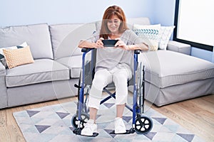 Middle age woman watching video on smartphone sitting on wheelchair at home