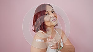 Middle age woman wearing band aid for vaccination doing thumb up gesture over isolated pink background