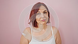Middle age woman wearing band aid for vaccination doing thumb up gesture over isolated pink background
