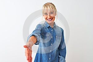 Middle age woman wearing casual denim shirt standing over isolated white background smiling friendly offering handshake as