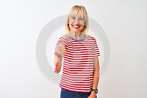 Middle age woman wearing casual striped t-shirt standing over isolated white background smiling friendly offering handshake as