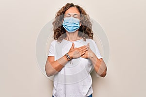 Middle age woman wearing coronavirus protection mask for covid-19 epidemic virus smiling with hands on chest, eyes closed with