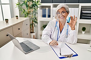 Middle age woman wearing doctor uniform holding inhaler at clinic