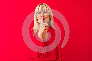 Middle age woman wearing elegant shirt standing over isolated red background asking to be quiet with finger on lips