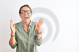 Middle age woman wearing green shirt and glasses standing over isolated white background celebrating mad and crazy for success