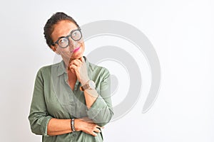 Middle age woman wearing green shirt and glasses standing over isolated white background with hand on chin thinking about