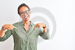 Middle age woman wearing green shirt and glasses standing over isolated white background looking confident with smile on face,