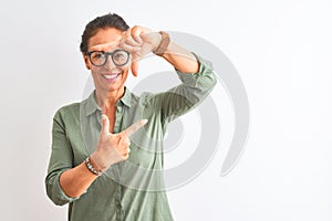 Middle age woman wearing green shirt and glasses standing over isolated white background smiling making frame with hands and