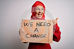 Middle age woman wearing muslim hijab asking for change holding banner pointing and showing with thumb up to the side with happy