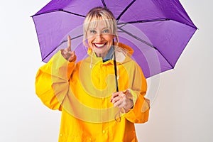 Middle age woman wearing rain coat and purple umbrella over isolated white background surprised with an idea or question pointing