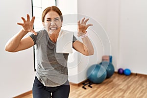 Middle age woman wearing sporty look training at the gym room smiling funny doing claw gesture as cat, aggressive and sexy