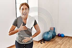 Middle age woman wearing sporty look training at the gym room smiling and laughing hard out loud because funny crazy joke with