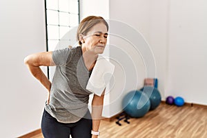 Middle age woman wearing sporty look training at the gym room suffering of backache, touching back with hand, muscular pain