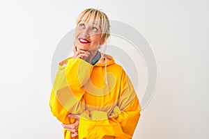 Middle age woman wearing yellow rain coat standing over isolated white background with hand on chin thinking about question,