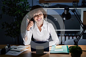 Middle age woman working at the office at night doing happy thumbs up gesture with hand