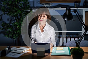 Middle age woman working at the office at night looking sleepy and tired, exhausted for fatigue and hangover, lazy eyes in the