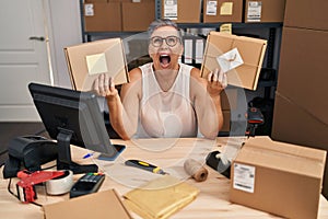 Middle age woman working at small business ecommerce angry and mad screaming frustrated and furious, shouting with anger looking